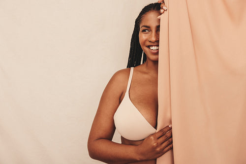 Gorgeous young woman smiling while standing behind a studio curtain