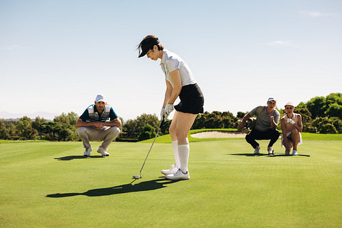 Woman in putting stance aiming carefully with players watching