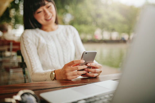 Asian female using cellphone at outdoor cafe