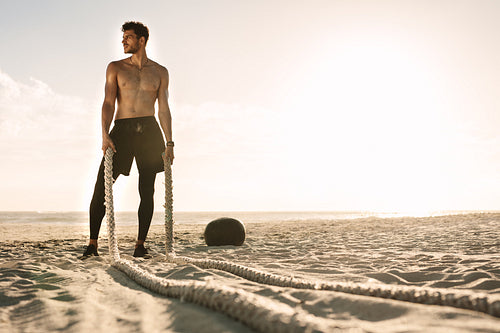 Man standing on the beach holding battling ropes for workout