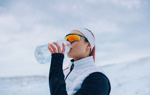 Woman pauses with water during winter running training in the cold outdoors