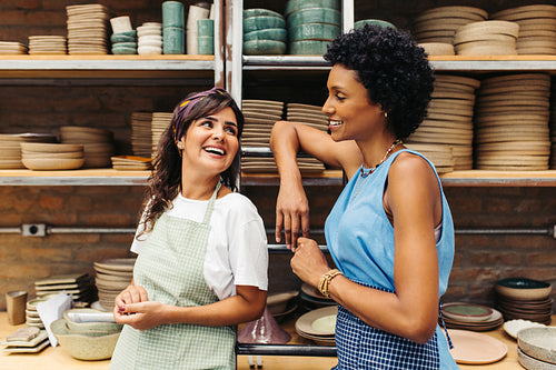 Cheerful female potters smiling at each other in their shop