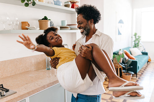 Mature black father carrying his daughter in a playful moment at home