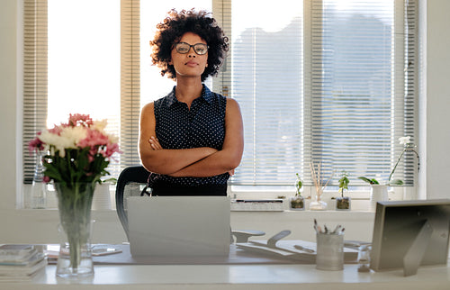 Confident young businesswoman standing at her desk