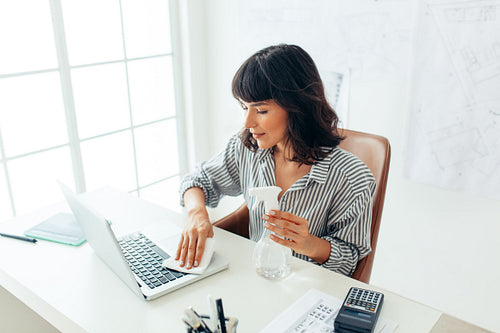 Businesswoman cleaning her laptop with sanitizer