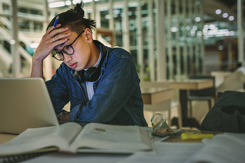 Depressed student sitting in library with laptop in college