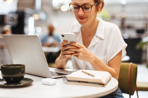 Business woman reading text message on smartphone while working remotely