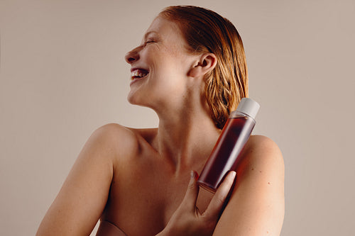 Woman with wet hair holding shampoo bottle, smiling