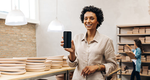 Cheerful ceramic shop owner showing a blank smartphone screen