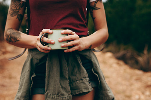 Woman holding a coffee mug while hiking in forest
