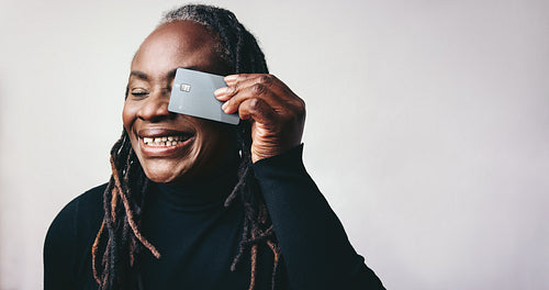 Cheerful mature woman smiling while holding a credit card in a studio