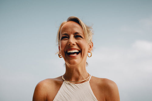 Smiling woman wearing gold jewelry against a clear sky background