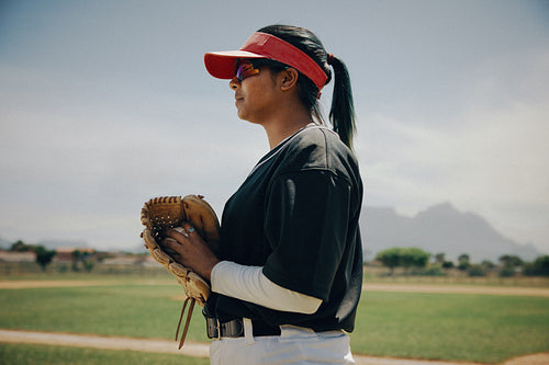 Female baseball pitcher holding leather mitt on the field, ready for action on a sunny day