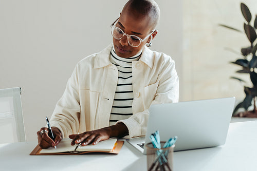 Focused business professional writing notes beside a laptop in her office