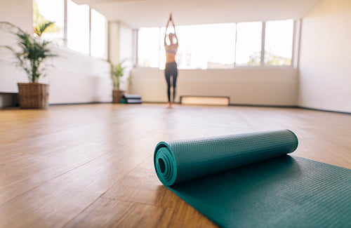 Exercise mat on floor with woman doing yoga