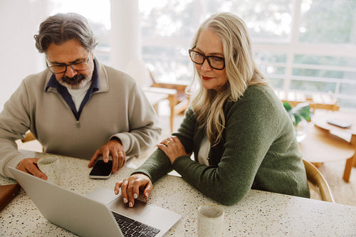 Senior couple use laptop and smartphone at home