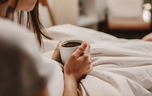Woman holding a coffee cup sitting on bed
