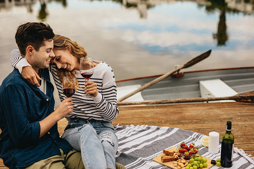 Couple on a date sitting together beside a lake drinking wine