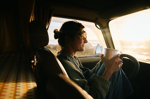 Woman in a cozy van at sunset enjoying a warm drink and road trip