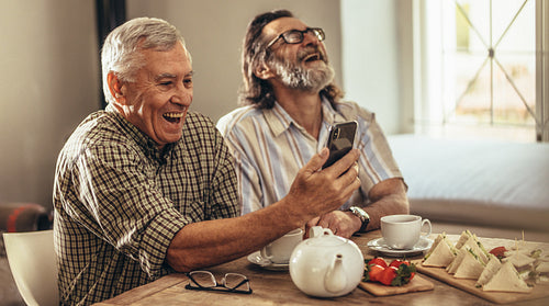 Retired men looking at old photographs on smartphone and laughing