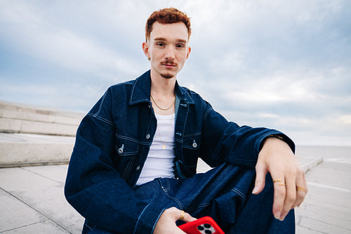 Young man in denim holding smartphone by steps