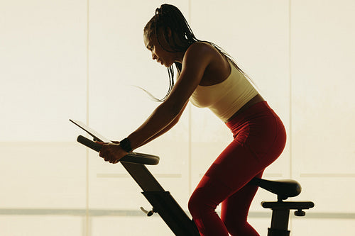 Fit woman in sports clothing using exercise bike for gym workout
