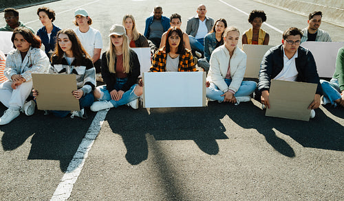 Diverse group of protestors sitting together holding blank cardboard signs outdoors