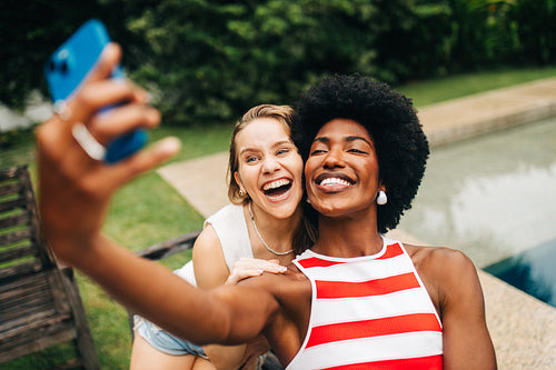 Two friends take a joyful selfie by the poolside