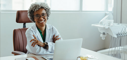 Smiling dentist using laptop at desk in bright dental office