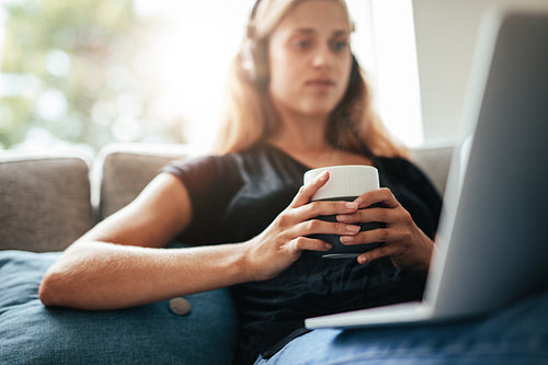 Cup of coffee in hands of a woman relaxing on sofa