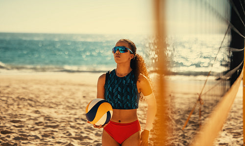 Female athlete playing beach volleyball at sunset on coastal sand court
