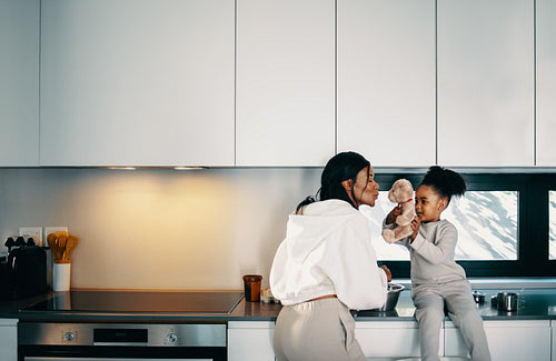 Mom playing with her daughter and her teddy bear in the kitchen