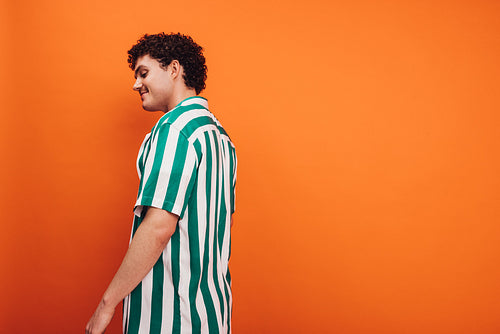 Cheerful queer man standing against an orange background