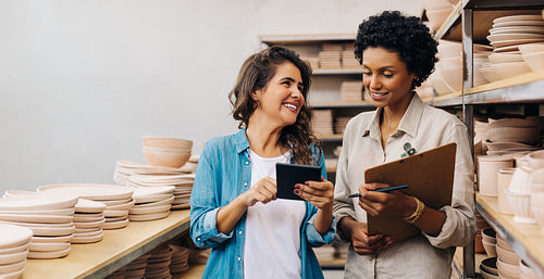 Two happy female ceramists working together in their shop