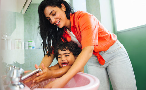 Mother helping her child wash hands in the bathroom sink