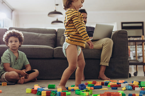 Kids playing at home with their father working on laptop