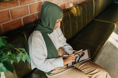 Young Muslim designer drawing on a digital tablet in a cafe