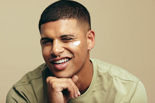 Fun skincare routine: Handsome young man smiles with beauty cream on his face