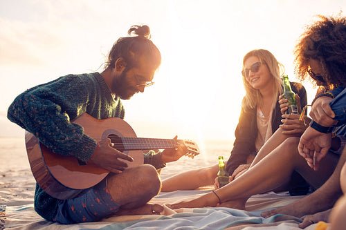 Young man playing guitar for friends on the beach