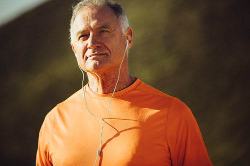 Close up of a senior man standing outdoors listening to music