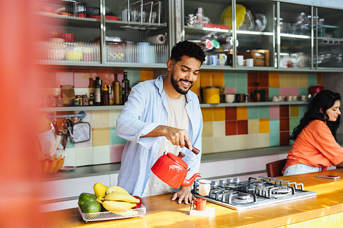 Latin American man pouring tea in a cozy colorful kitchen while preparing for breakfast