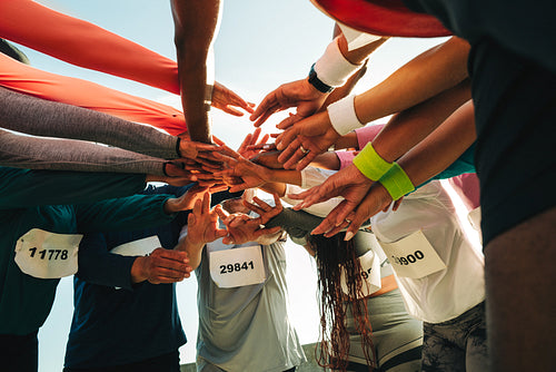 Group of runners joining hands in team spirit huddle