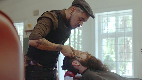 Hairdresser styling beard with scissors at barbershop
