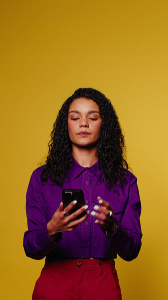 Young woman laughs at phone on yellow background