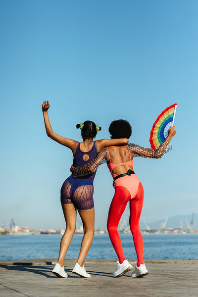 Two dancers embrace on waterfront in carnival outfits