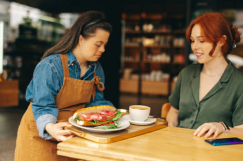 Waitress with Down syndrome serving a customer food in a cafe