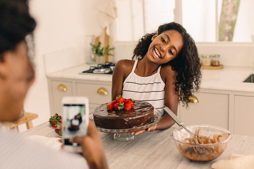 Girl with freshly baked cake being photographed by mother