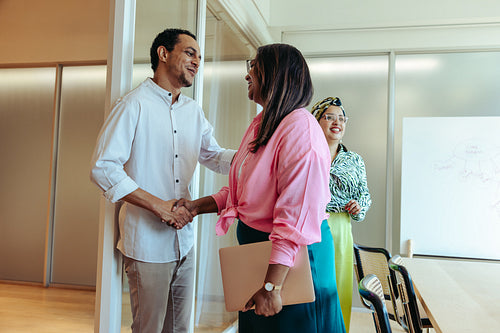 Colleagues sharing a handshake and smiling as a farewell gesture in a modern meeting room
