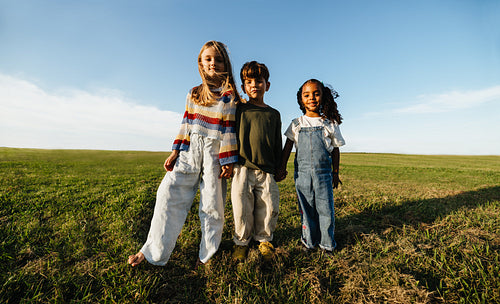 Three young children stand together in a field