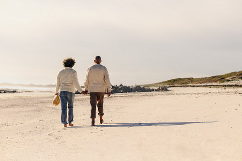 Rearview of an elderly couple walking barefoot on beach sand